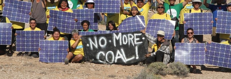 Group sits holds solar panels and sign that says "No More Coal"