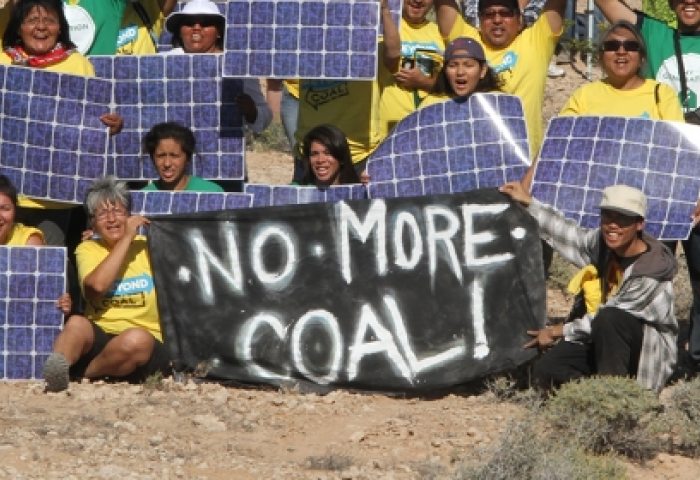 Group sits holds solar panels and sign that says "No More Coal"